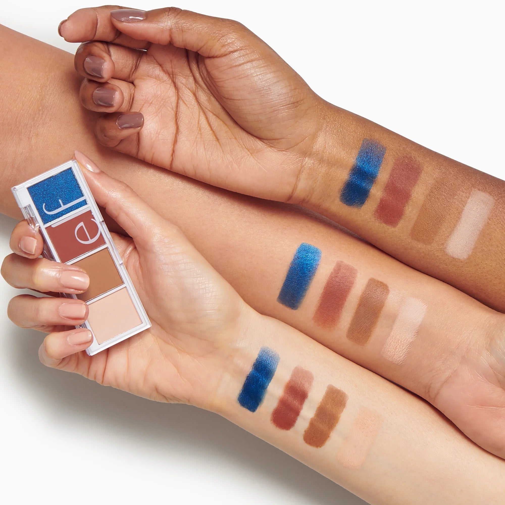 Makeup swatches on a person's arm with a makeup palette held by another hand.
