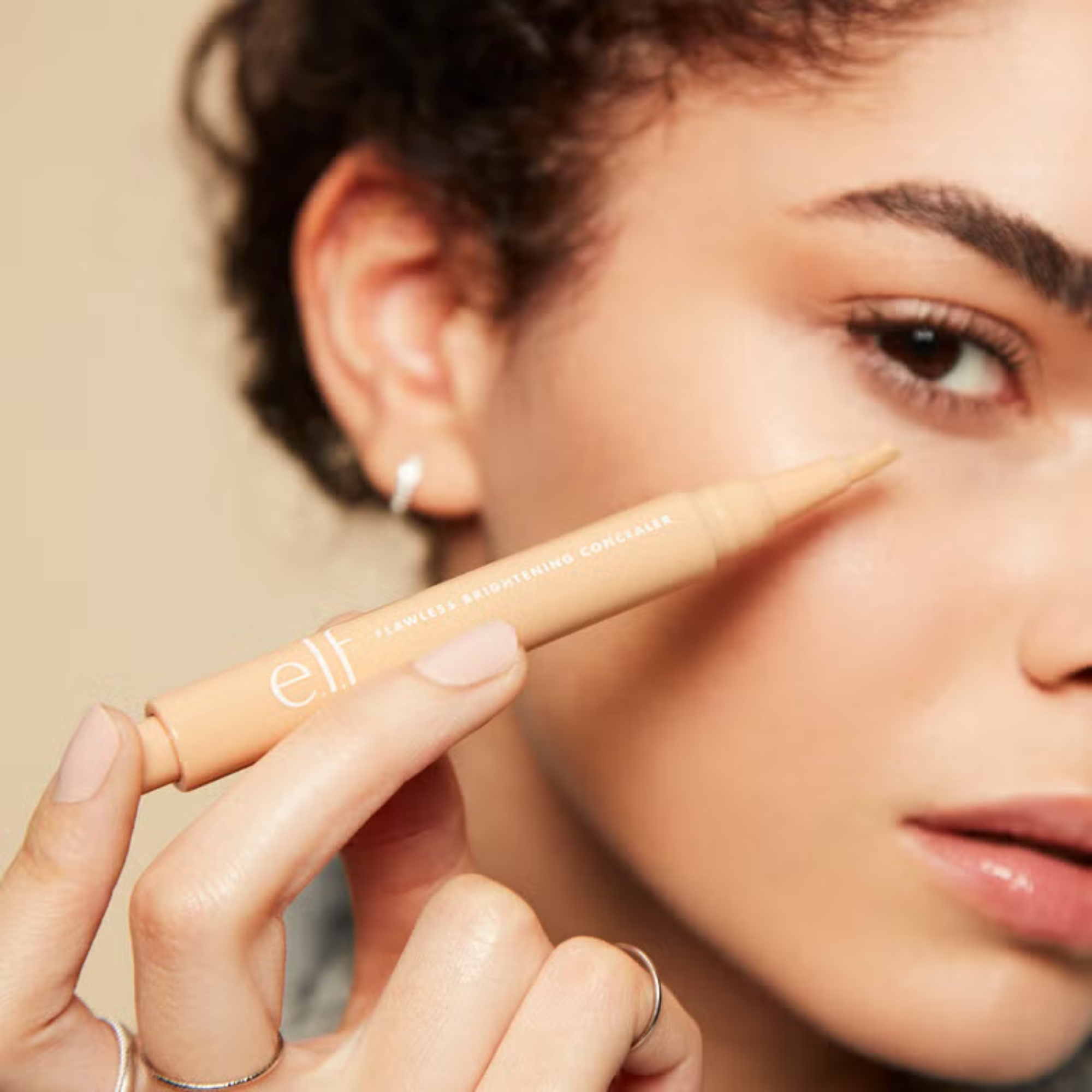 Person holding an 'elf' cosmetic pencil near their face against a neutral background