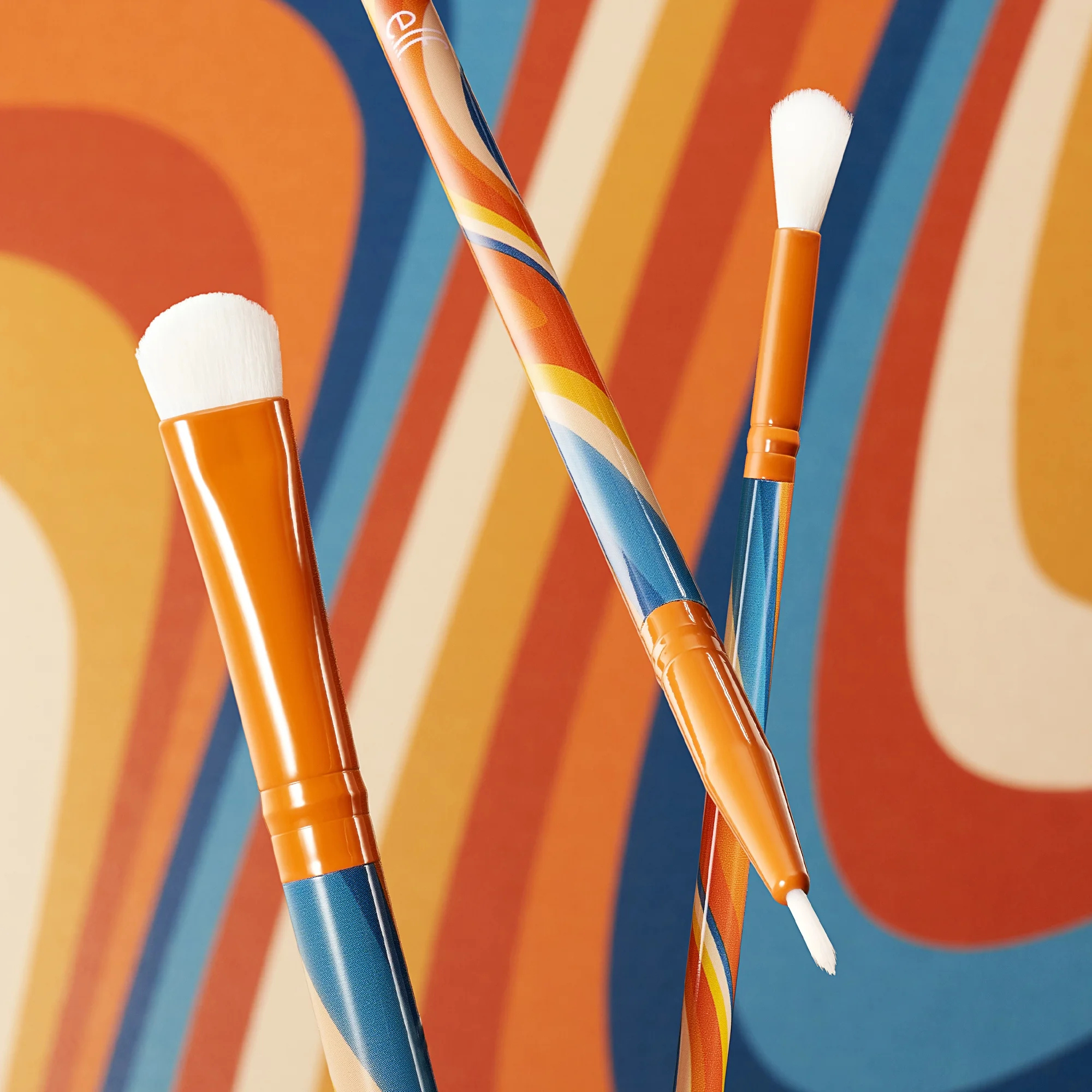 Two make up brushes with orange and blue handles on a colorful abstract background