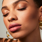 Close-up of a woman's face wearing luminous putty bronzer with gold hoop earrings against a neutral background