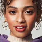 Close-up of a woman wearing hoop earrings and putty blush with a neutral background