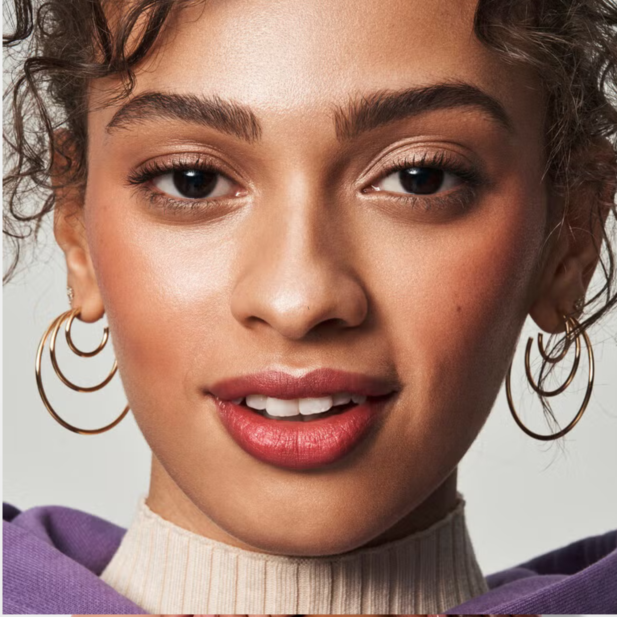 Close-up of a woman wearing hoop earrings and putty blush with a neutral background