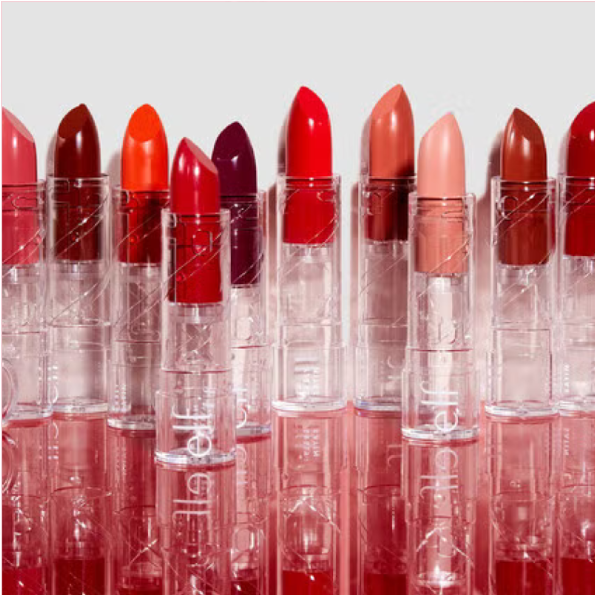 Row of lipsticks in various colors with clear casings on a light gray background